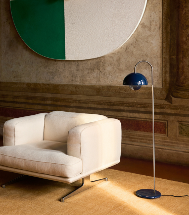 Elegant &Tradition gulvlampe ved siden av moderne loungestol i varmt interiør.