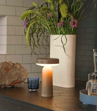 Bærbar Muuto bordlampe på mørk kjøkkenbenk med blomsterdekorasjon.
