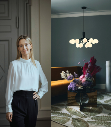 Portrett av designer Sofie Refer ved siden av en lysende pendellampe fra Nuura i et stilrent interiør med blomsterinnslag.