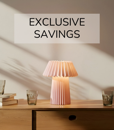 Blekrosa bordlampe på en skjenk av tre, omgitt av glass og bøker i det varme sollyset.