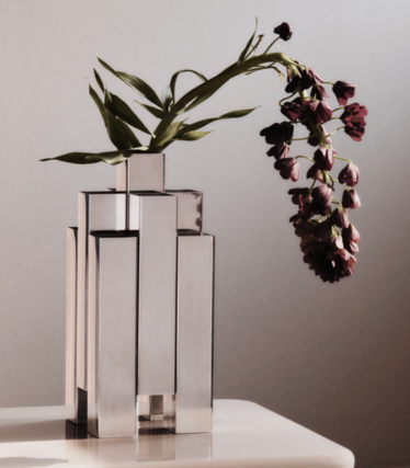 Skulpturell vase i polert rustfritt stål fra Ferm Living med mørkerøde blomster