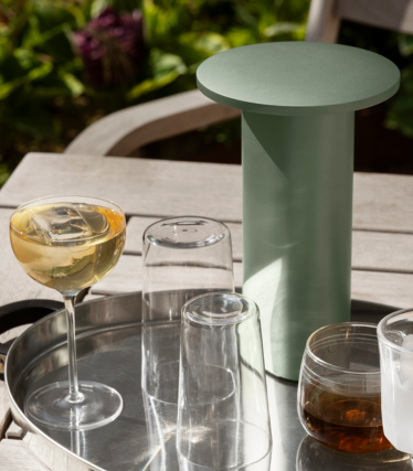 Salviegrønt, sylindrisk sidebord/kjøler på et brett med glass og drikkevarer utendørs.